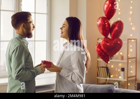 Glücklicher, gutaussehender junger Mann schenkt seinem attraktiven Liebhaber ein Geschenk zum Valentinstag, Geburtstag, Feiertag. Stockfoto