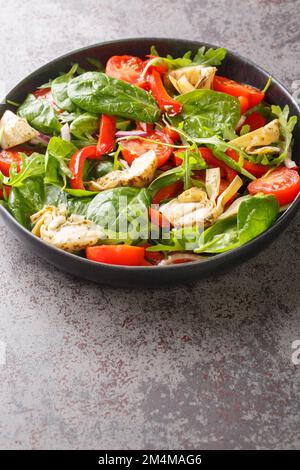 Diätetischer Salat mit eingelegten Artischocken, Tomaten, Spinat, Rucola, gebratenen Paprika und Zwiebeln in Nahaufnahme auf einem Teller auf dem Tisch. Vertikal Stockfoto