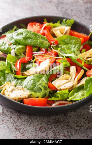 Frischer Salat mit Artischocken, Tomaten, Spinat, Rucola, gebratenen Paprika und Zwiebeln in Nahaufnahme auf einem Teller auf dem Tisch. Vertikal Stockfoto