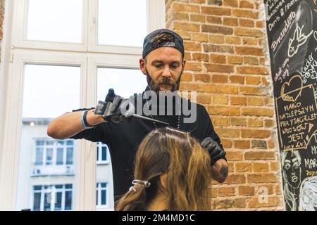 Nachwuchsbehaarung. Fokussieren Sie den Haarexperten, der das braune Haar seines Kunden mit Haarfärbemittel oder Bleichmittel behandelt. Männlicher Kaukasier-Friseur. Hochwertiges Foto Stockfoto