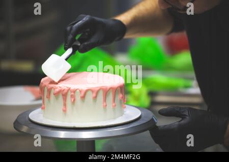 Kuchenkoch-Designer mit Spachtel, um rosa Tropfen auf weißen Milchkuchen zu glätten und zu glätten, um Geburtstagsfeiern für kleine Mädchen im Küchenlabor zu feiern Stockfoto