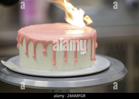 Der Kuchenkoch-Designer bereitet im Küchenlabor einen rosafarbenen, auf weißen Milchkuchen tropfenden Kuchen für die Geburtstagsfeier des kleinen Mädchens zu Stockfoto