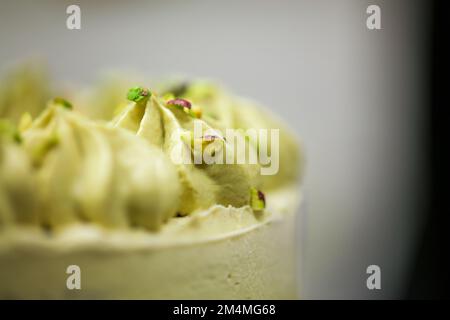 Der Konditoreidesigner streut den grünen, mattierten Schokoladenkuchen mit kleinen pistacchio- und dunklen Schokoladenstücken Stockfoto