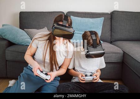 Mutter und Sohn genießen gemeinsam Entertainment-Videospiele mit VR-Brillen und -Controllern, während sie auf dem Sofa im Wohnzimmer sitzen Stockfoto
