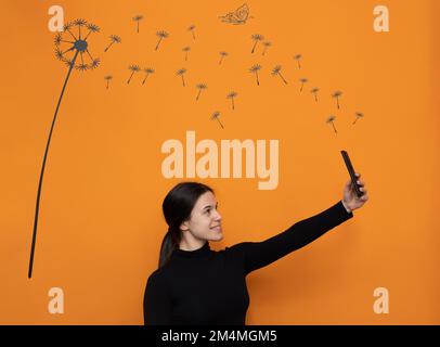 Seitenansicht wunderschöne glückliche weiße Frau halten Sie Ihr Mobiltelefon hoch Selfie mit orangefarbenem Hintergrund Sau-Distel Illustration .Kreativität, positive Vibes Stockfoto