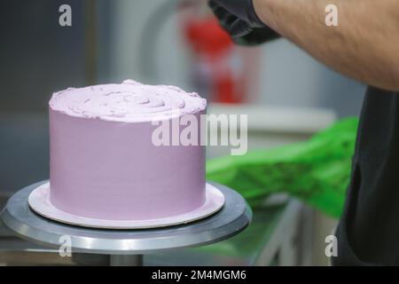 Konditorin mit Spatel und Schaber, glättend, lila Buttercreme, Milchkuchen - Zubereitung von Hochzeitstorten Stockfoto