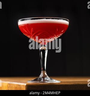 Roter Cocktail in Coupé-Glas mit Schaumschicht auf schwarzem Hintergrund. Stockfoto