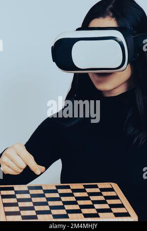 Nahaufnahme Porträt aufgeregte weiße Frau trägt VR-Set und spielt Schach in isoliertem Hintergrund. Virtual-Reality-Spiele und Metaverse-Experience-Konzept Stockfoto