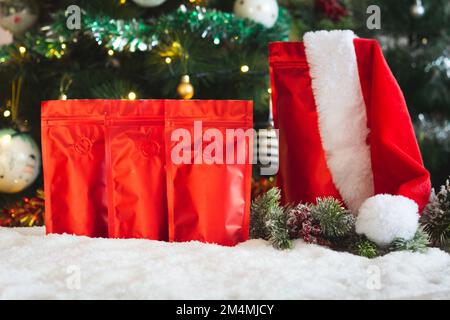 Leere Kaffeepackung auf dem Hintergrund des Weihnachtsbaums, Weihnachtsmannmütze, künstlicher Schnee, Kaffeepackung mit leerem Platz zum Ausstellen Stockfoto