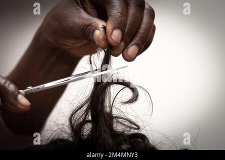 Nahaufnahme der Hände einer afrikanischen Frau, die einem Kind die Haare schneidet, für ein Hexenritual. Konzept der schwarzen Magie und Voodoo-Riten. Foto isoliert Stockfoto