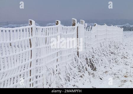 Ein weißer Zaun mit Schnee in einem ländlichen Gebiet im kalten Winter, Deutschland Stockfoto