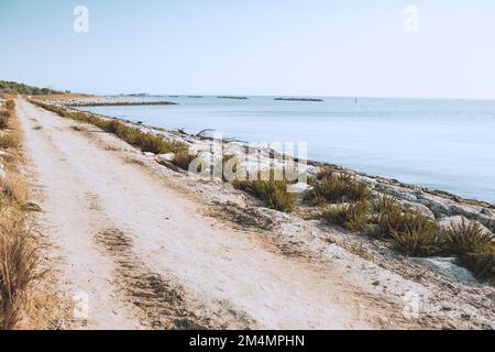 Panoramablick auf den Strand mit blauem Wasser und Pflanzen entlang der Straße und klarem blauen Himmel und ohne Menschen. Ruhige Küste in Europa Stockfoto