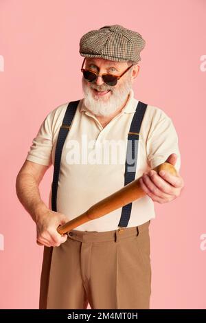 Porträt eines Seniorenmannes in klassischer Kleidung, Mütze, Hosenträger und Sonnenbrille mit Fledermaus auf rosa Hintergrund. Geschäftsmann Stockfoto
