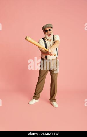 Porträt eines stilvollen Seniorenmannes in klassischer Kleidung, Mütze und Sonnenbrille mit Fledermaus auf pinkfarbenem Hintergrund. Servieren Stockfoto