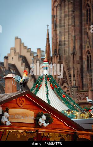 STRASSBURG, FRANKREICH - 2018. Dezember - Weihnachtsmarkt Chalets mit Brezel und Hahn vor der Kathedrale und Karussell in Straßburg Stockfoto