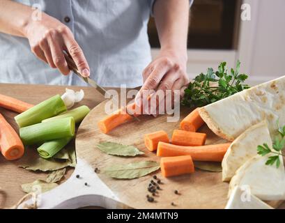 Von oben von der Ernte anonyme Frau schneidet frische Karotten mit Messer auf Holzbrett, während sie ein gesundes Mittagessen in der Küche zubereitet Stockfoto