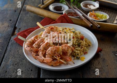 Von oben gibt es köstliche Shrimps, die auf Spießen mit Nudeln auf einem Teller neben dem Tablett serviert werden, mit Saucen in einem hellen Restaurant Stockfoto