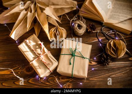 Hausgemachtes Weihnachtsbaumspielzeug zu Weihnachten. Das Konzept der Verpackung von Geschenken in Handwerkspapier. Ein großer Weihnachtsstern aus Papier auf einem alten Holztisch. Stockfoto