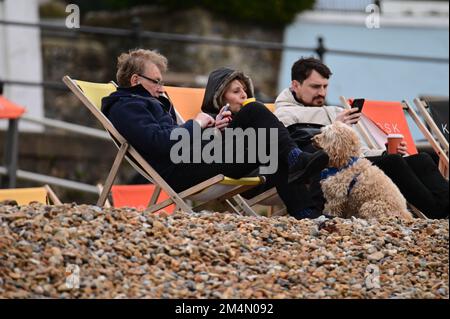 Lyme Regis, Großbritannien. 22. Dezember 2022. An einem feuchten und kalten Tag im Lyme Regis in East Devon werden Menschen gesehen, die in Liegestühlen an einem Kieselstrand sitzen, sich entspannen und die Flut beobachten. 3 Tage vor Weihnachten. Bildnachweis: Robert Timoney/Alamy Live News Stockfoto