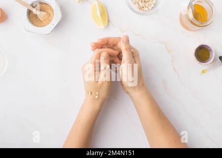 Flatlay mit hausgemachten Kosmetikprodukten: Frische Zutaten wie Hafer, Honig, Zitrone, Banane, Ei, Olivenöl. Weibliche Hand mit einem Glas Sahne. Gemeinkosten Stockfoto