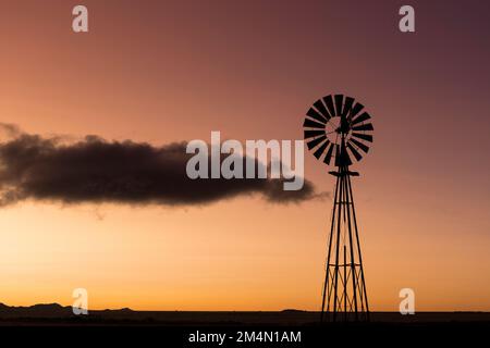 Die Silhouette einer Windmühle bei Sonnenuntergang mit einem orangefarbenen Himmel und einer dunklen Wolke, die vorbeizieht. Stockfoto