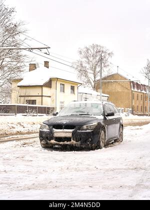 Riga, Lettland - 13. Dezember 2022: Gefrorenes BMW-Auto mit Eisschicht überzogen am Wintertag auf der Straße der Stadt geparkt. Vertikaler Schuss. Stockfoto