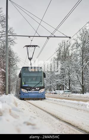 Riga, Lettland - 13. Dezember 2022: Moderne Straßenbahn auf der verschneiten Winterstraße. Vertikaler Schuss. Stockfoto