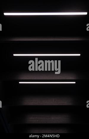 Eine große, moderne schwarze Holztreppe mit weißen LED-Lichtern Stockfoto