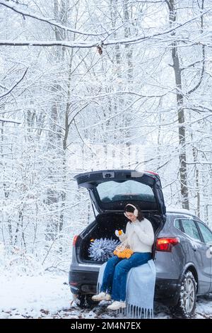Mitten in einem Winterwald, eine junge Frau in einem Auto mit einem Weihnachtsbaum Stockfoto