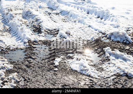 Schmelzen von Schnee und Schlamm mit Autoreifen auf einer unbefestigten Straße, die von den Strahlen der hellen Sonne erleuchtet wird. Stockfoto