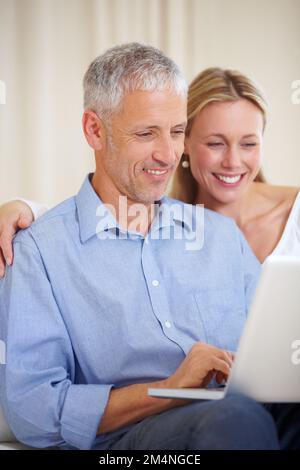 Das Internet ist eine großartige Möglichkeit, um in Kontakt zu bleiben. Ein verheiratetes Paar, das mit seinem Laptop sitzt. Stockfoto