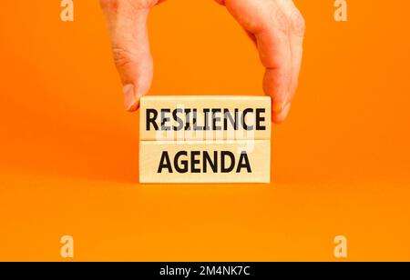 Symbol für Resilienz-Agenda. Konzeptwort „Resilience Agenda“ auf Holzblöcken getippt. Schöner orangefarbener Tischhintergrund. Geschäftsmannshand. Geschäftlich Stockfoto