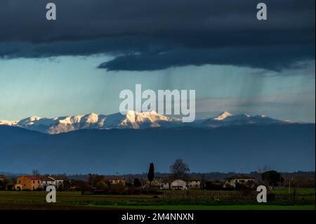 Schwarze Wolken und Regen über der Landschaft, mit schneebedeckten Bergen im Hintergrund, Bientina, Pisa, Italien Stockfoto