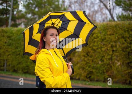 Ein Mädchen in Gelb mit gestreiftem Regenschirm Stockfoto