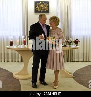 Ältere Ehepaare an ihrem Hochzeitstag. Der Mann hält eine brennende Kerze und die Frau hält einen Strauß. Stockfoto