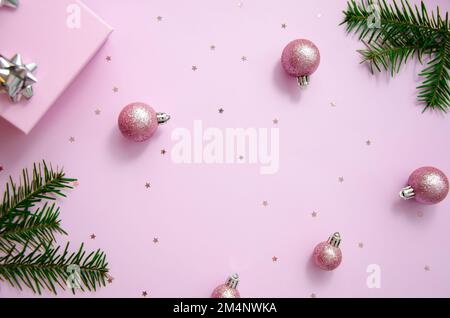 Weihnachtskomposition. Pinkfarbene Kugeln, hölzerne Schneeflocken, Tannenäste, Glitzer, Geschenkbox auf pastellrosa Hintergrund. Weihnachten, Winter, Neujahrskonzept. F Stockfoto