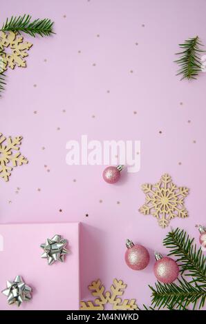 Weihnachtskomposition. Pinkfarbene Kugeln, hölzerne Schneeflocken, Tannenäste, Glitzer, Geschenkbox auf pastellrosa Hintergrund. Weihnachten, Winter, Neujahrskonzept. F Stockfoto