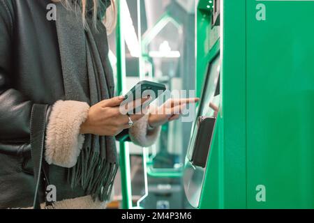 Drahtlose, kontaktlose Kartenzahlung. Eine junge weiße Frau nimmt ihr aufgefülltes Ticket von einem Terminal. Ein Mädchen, das ohne Zugeständnisse mit Bankkarte bezahlt Stockfoto