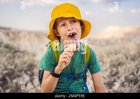 Tourismusjunge, der türkisches Eis isst, während er das Tal mit Felsformationen und Feenhöhlen in der Nähe von Goreme in Kappadokien, Türkei, erkundet Stockfoto