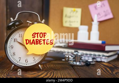 Medizinisches Konzept. Auf dem Wecker ein Aufkleber mit der Aufschrift "STOP DIABETES". Im Hintergrund, unscharf, gibt es ein Stethoskop, ein Nasenloch Stockfoto