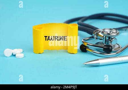 Medizinisches Konzept. Auf einer blauen Oberfläche, einem Stethoskop, Pillen, einem Stift und einem gelben Schild mit der Aufschrift - Taurine Stockfoto