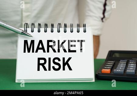 Geschäftskonzept. Auf einer grünen Oberfläche befindet sich ein Taschenrechner, ein Mann zeigt mit einem Stift auf ein Notizbuch mit der Aufschrift "Marktrisiko" Stockfoto