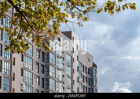 Moderne Fassadenarchitektur in einem Wohngebäude in sonnigen Ästen. Graue Wände mit blauen Fenstern am bewölkten Himmel Stockfoto