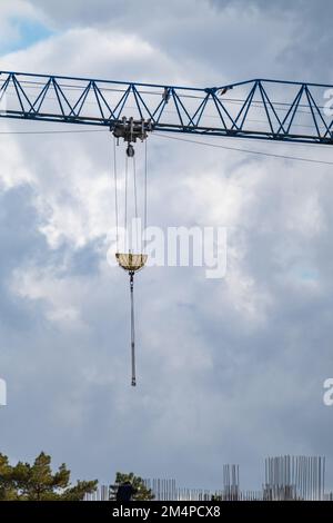 Blauer, hoher, überstehender Kranarm zum Heben großer schwerer Gewichte auf der Baustelle auf bewölktem, landschaftlich schönen Himmelshintergrund Stockfoto