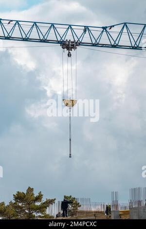 Blauer, hoher Kragarm zum Heben schwerer Gewichte auf der Baustelle eines mehrstöckigen Gebäudes mit bewölktem, landschaftlich schönen Himmelshintergrund Stockfoto