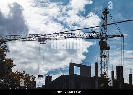 Hoher vorstehender Kranarm zum Heben schwerer Gewichte auf der Baustelle eines mehrstöckigen Gebäudes mit bewölktem, landschaftlich schönen Himmelshintergrund Stockfoto