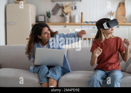 Mutter schaut Tochter Tochter Tochter an und erforscht virtuelle Realität als Zuhause. Familien und neue Technologien Stockfoto