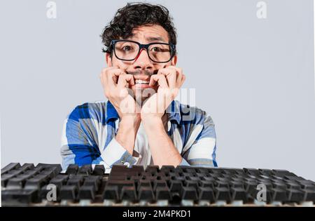 Nervöser Streber, der sich vor der Tastatur die Nägel beißt, besorgter Mann mit Brille an der Computertastatur. Ein junger Mann, der sich vor ihm Sorgen macht Stockfoto