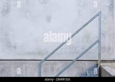 Das graue Treppengeländer vor einer ebenso grauen, verwitterten Wand hat einen minimalistischen, grafischen und gleichzeitig abstrakten Effekt. Stockfoto