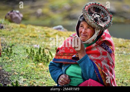 Quechua-Indianerin in traditionellen Kleidern sitzt auf einer Wiese und raucht bei der Pacha-Mama-Zeremonie, Anden, Ollantaytambo, Urubamba-Tal, in der Nähe von Cusco Stockfoto